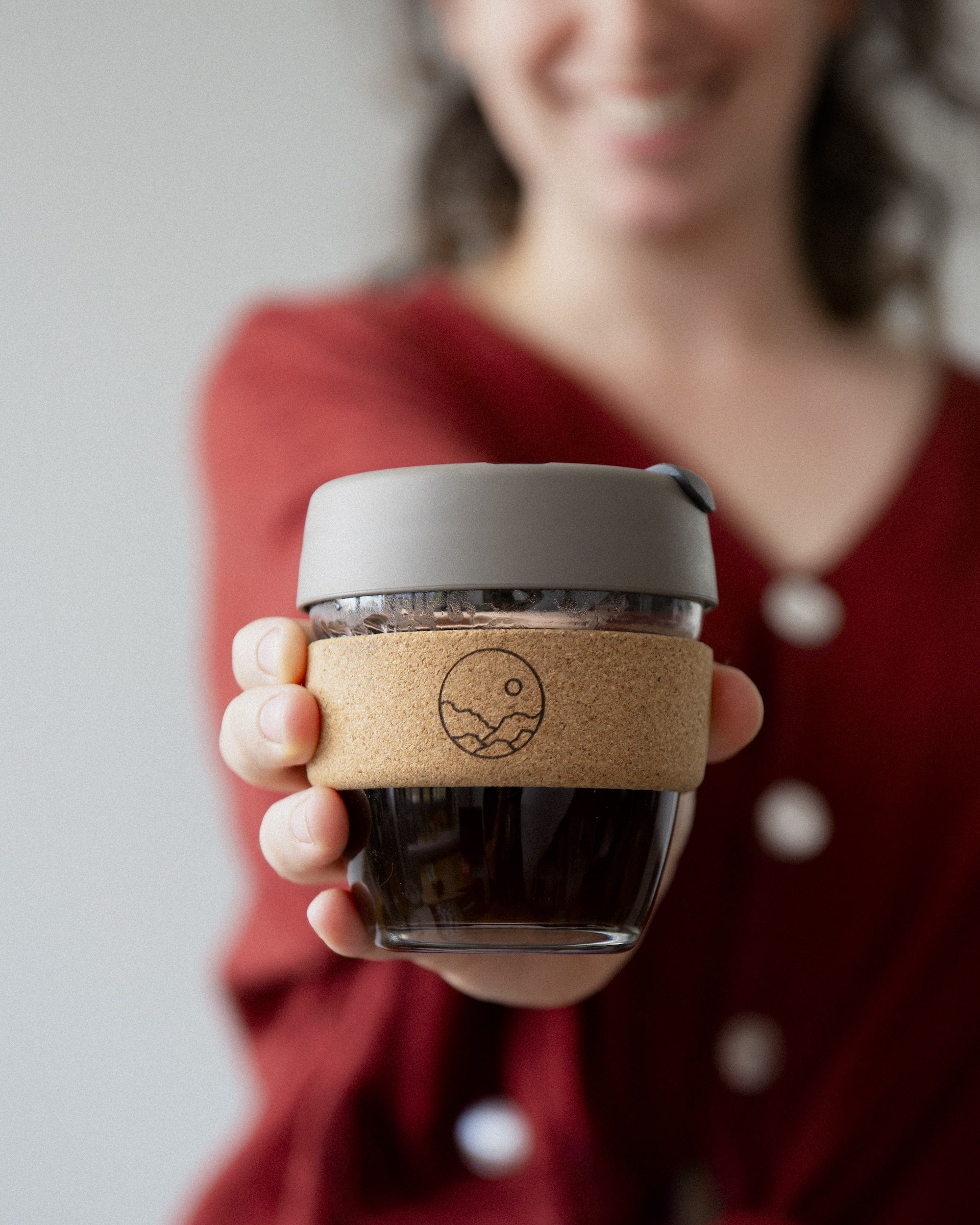 An individual holding a Keep Cup, a glass takeaway coffee cup with a cork heat-proof band.